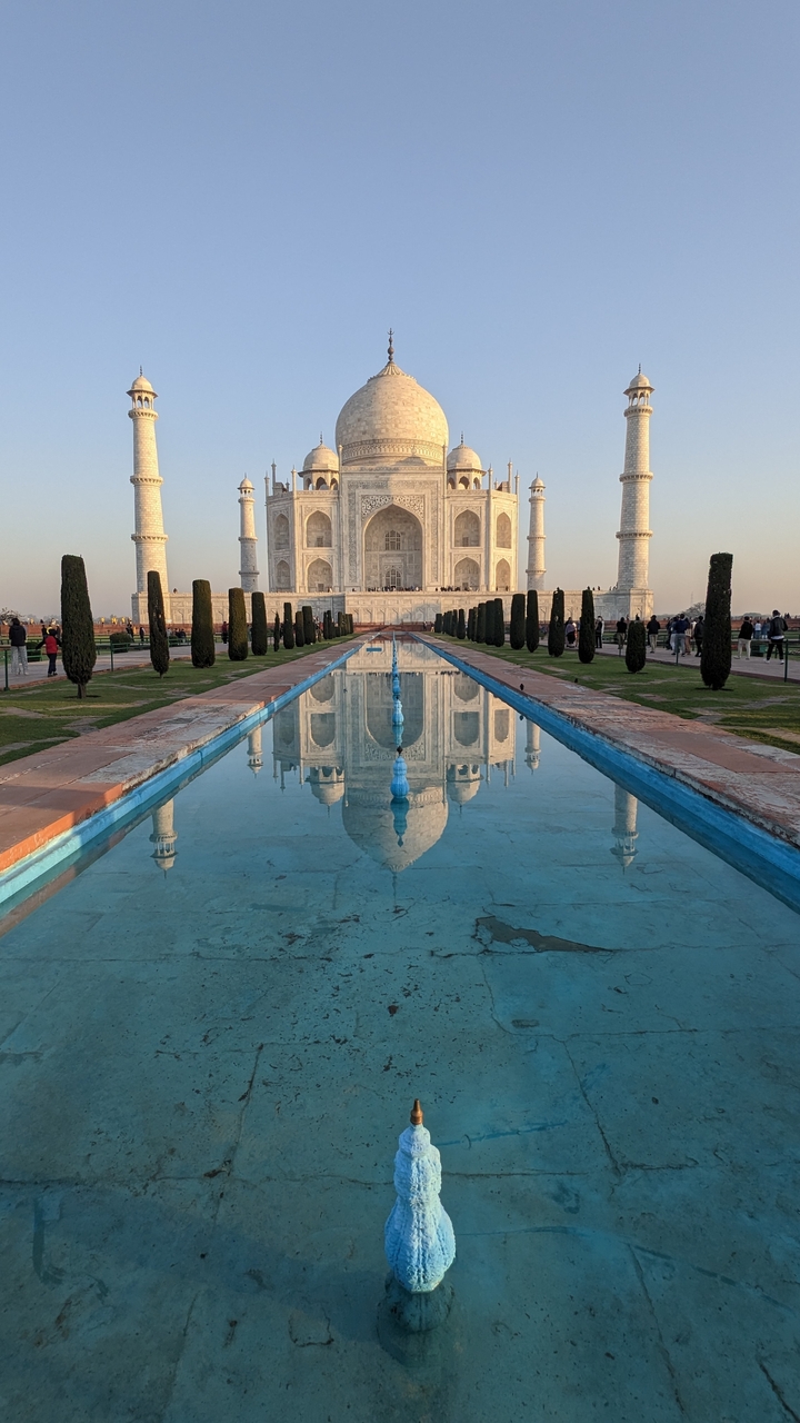 Le Taj Mahal se reflétant dans un long bassin d'eau sous un ciel dégagé.