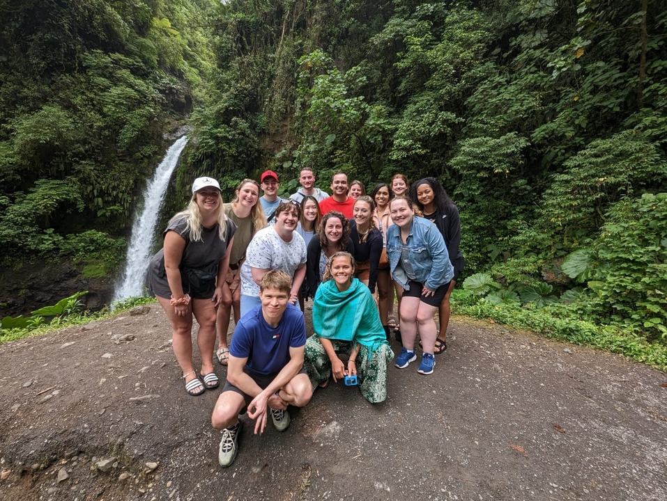 Un groupe de touristes posant devant une cascade dans un cadre forestier.