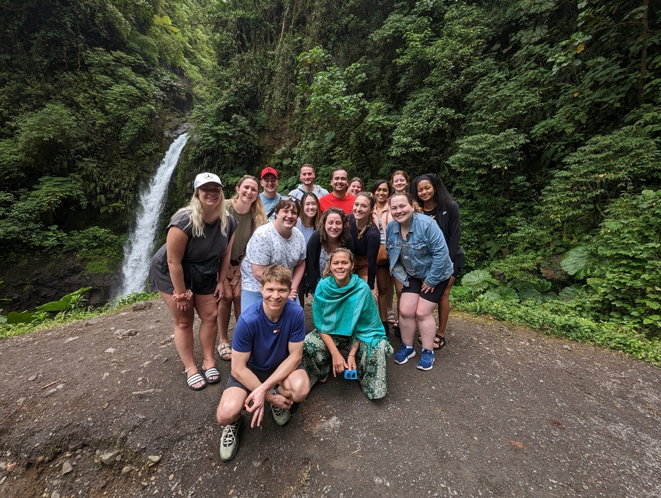 Un groupe de touristes posant devant une cascade dans un cadre forestier.