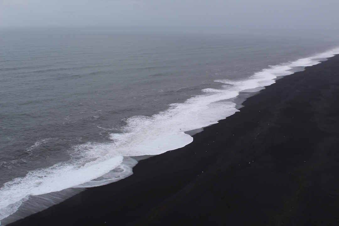 Plage de sable noir avec des vagues qui se brisent sur le rivage.