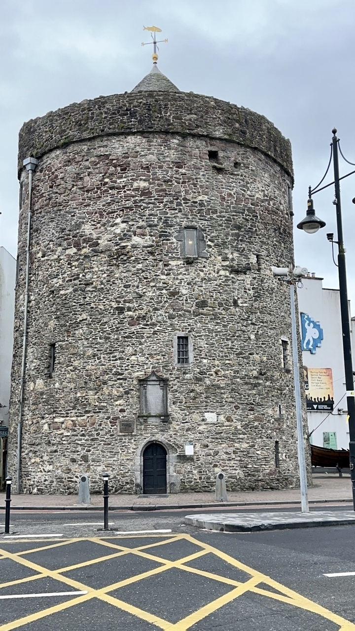 Un bâtiment en pierre rond avec une porte et de petites fenêtres, possiblement une ancienne tour.