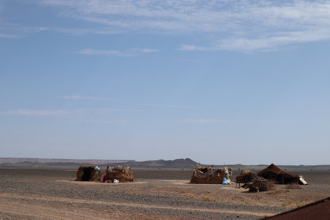 A view of simple desert huts on a flat, barren landscape under a clear sky.