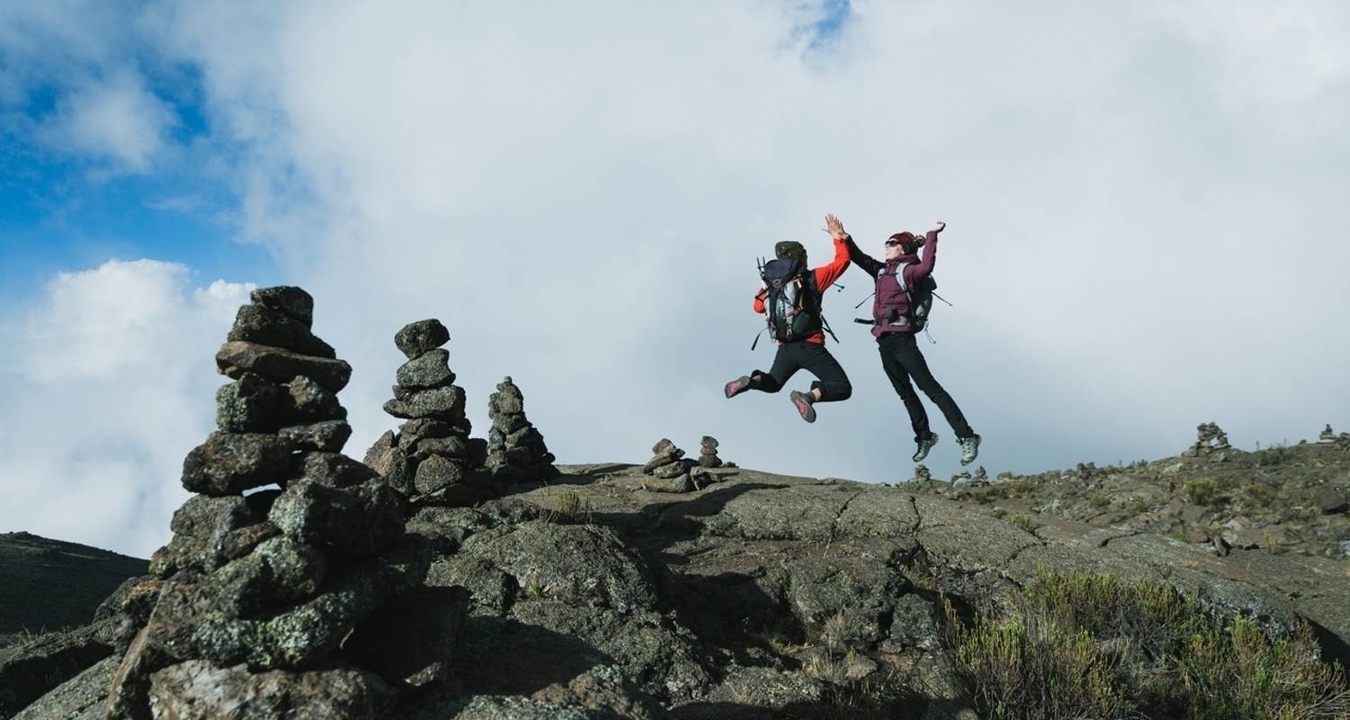 Deux personnes sautent sur un sentier de montagne rocailleux.