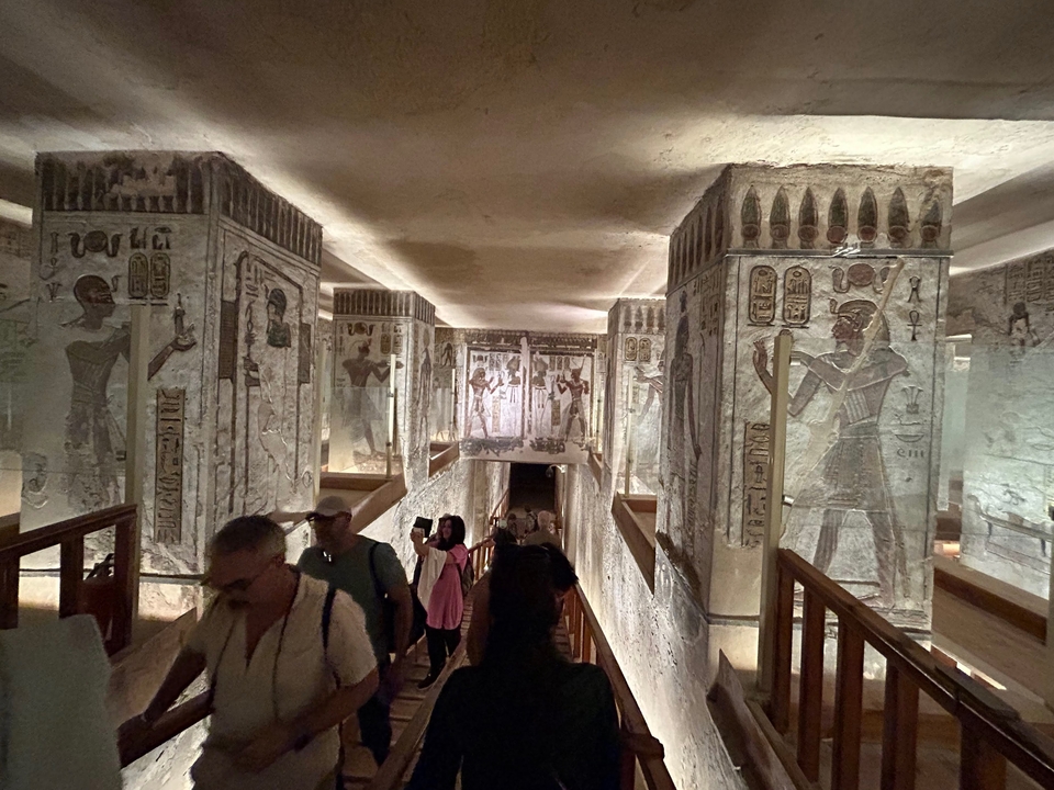 Couloir à l'intérieur d'un temple avec des hiéroglyphes et des touristes qui marchent.