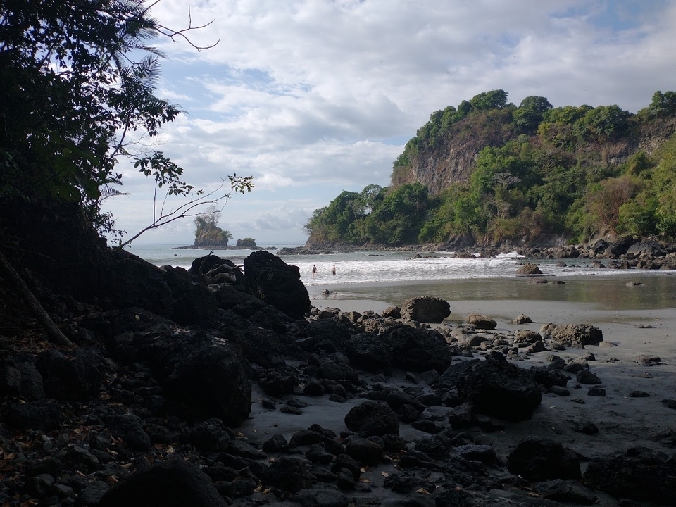 Scène de plage côtière avec formations rocheuses et personnes qui nagent.