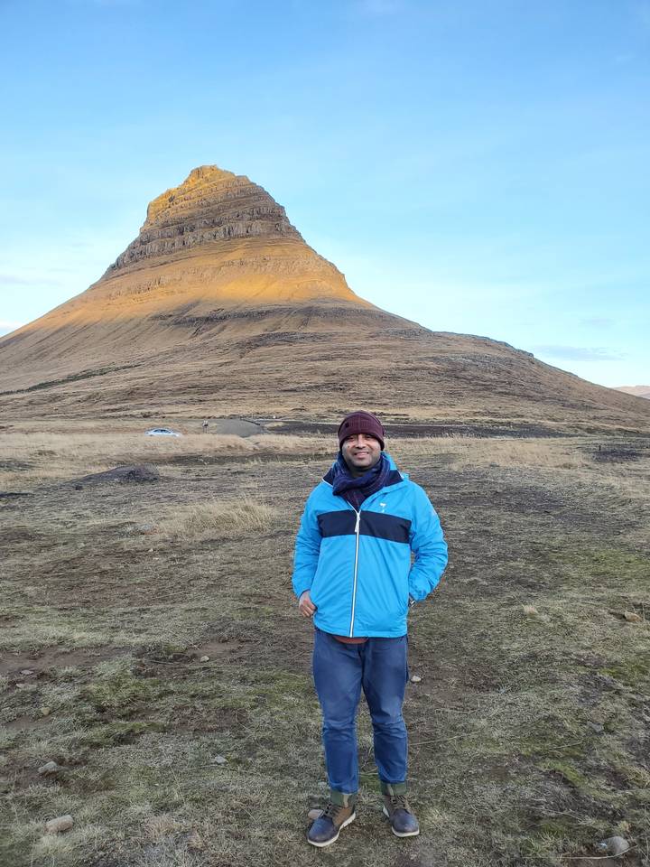 Person standing in front of a mountain under blue sky.