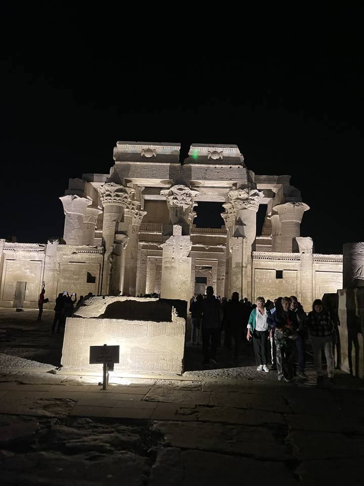 Temple ancien illuminé la nuit avec des gens autour.