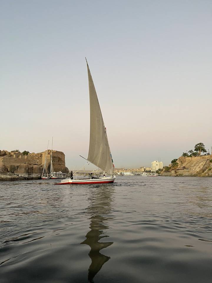 Bateau à voile traditionnel sur une rivière avec paysage en arrière-plan.