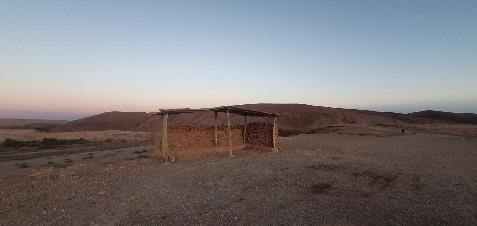 Un simple abri en bois avec des collines en arrière-plan au crépuscule.