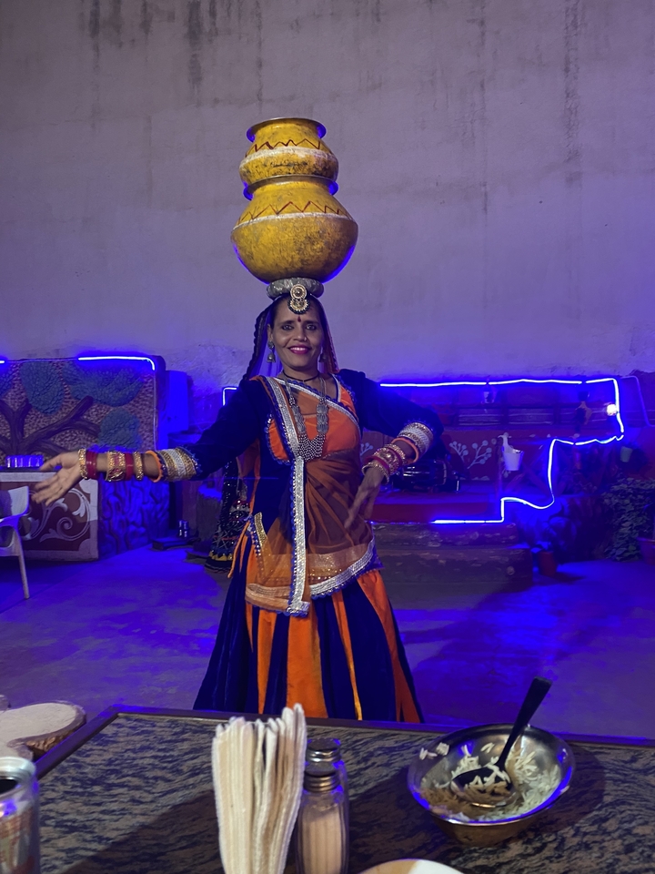 Danseur traditionnel en tenue colorée exécutant une danse avec un pot sur la tête.