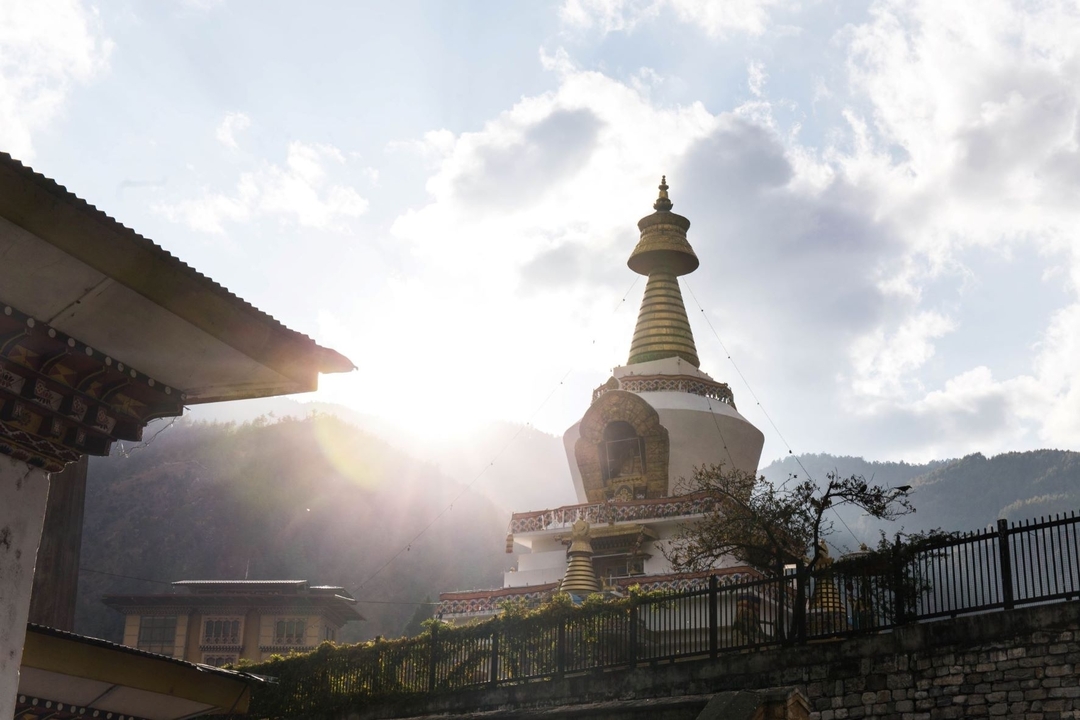 Stupa bouddhiste avec drapeaux de prière et soleil brillant derrière.