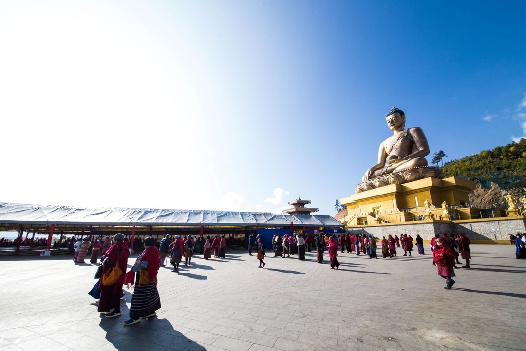 Grande statue de Bouddha sur une plateforme avec des personnes en robes traditionnelles.