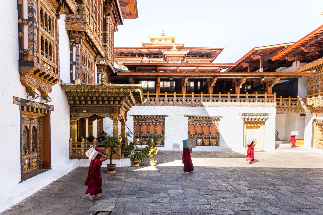 Moines marchant dans une cour traditionnelle bhoutanaise.