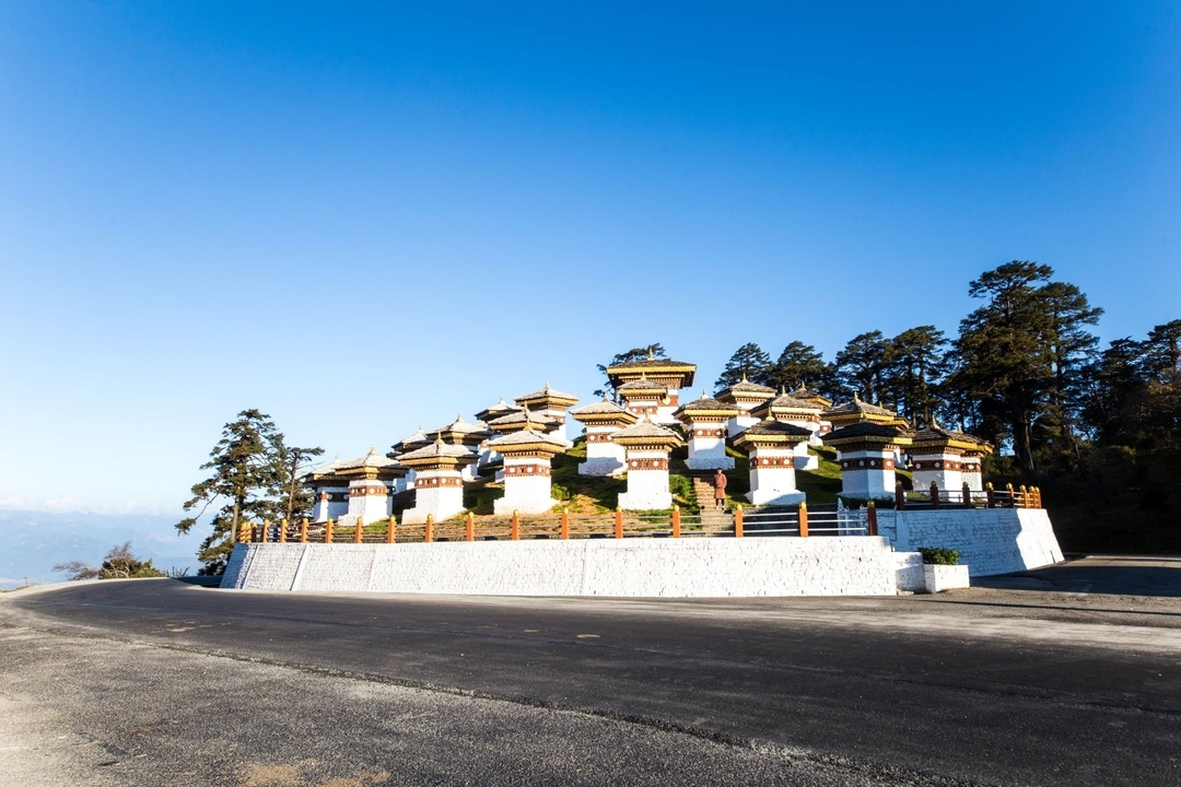 Groupe de stupas sur une colline avec un ciel bleu dégagé et un arrière-plan montagneux.