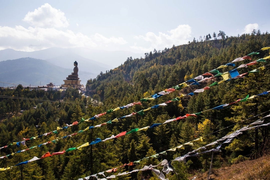 Flanc de montagne avec des drapeaux de prière colorés et un grand Bouddha au loin.