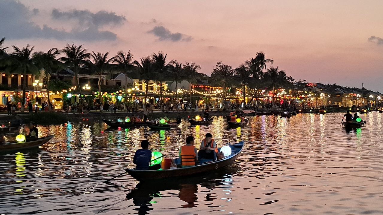 Bateaux sur une rivière avec des lumières colorées au crépuscule.