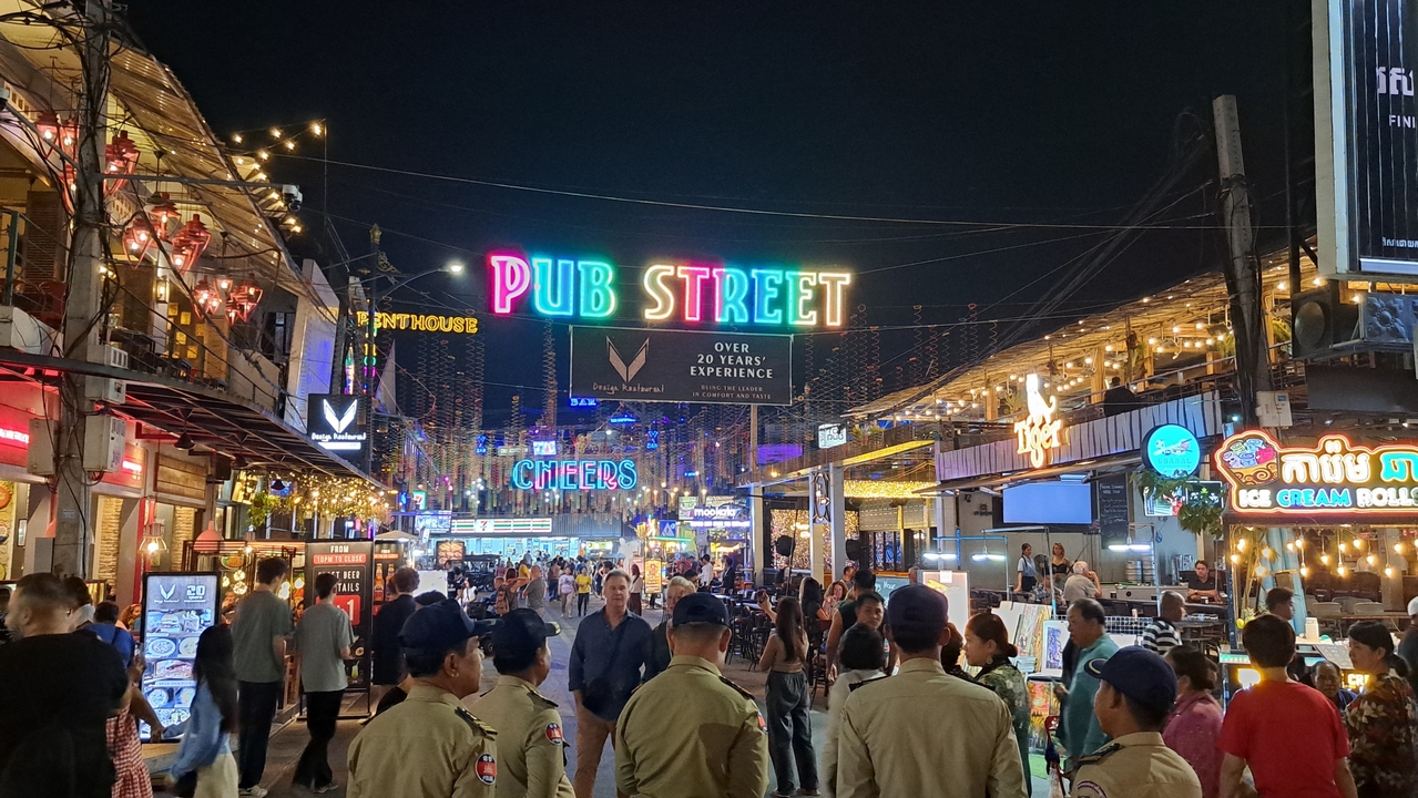Rue animée de la vie nocturne avec des enseignes lumineuses et des foules.