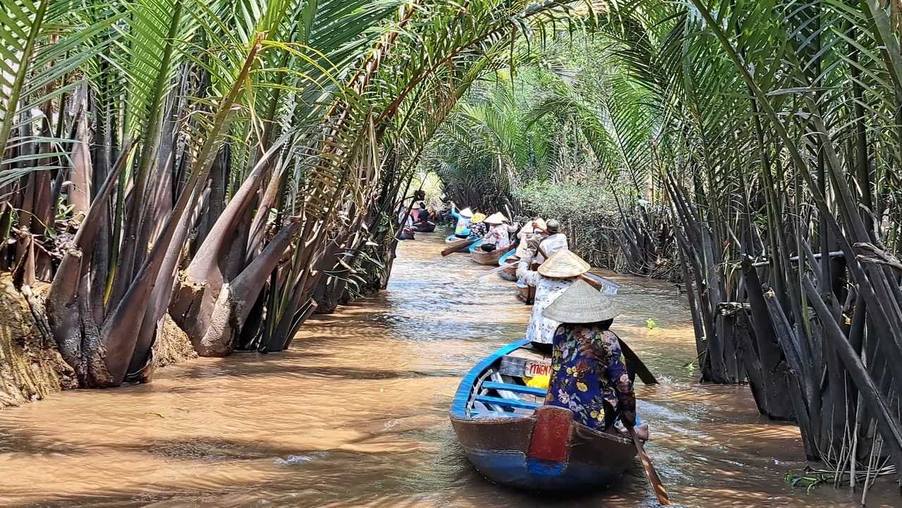 Des touristes sur de petites embarcations dans un canal étroit et luxuriant.
