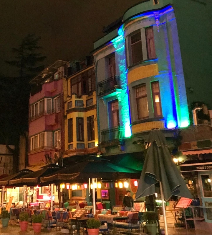 Bâtiments colorés éclairés la nuit avec des terrasses de restaurant.