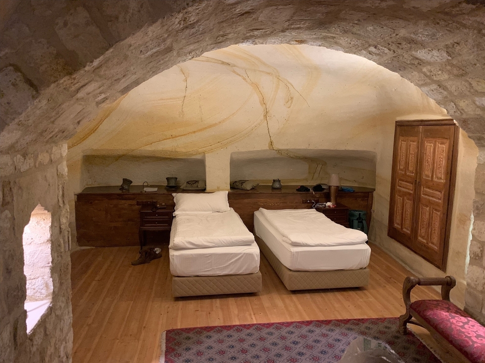 Configuration de chambre troglodyte avec deux lits et mobilier rustique.
