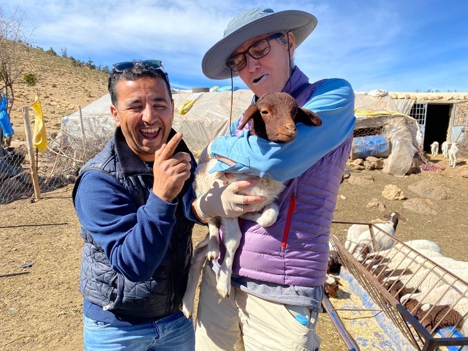 Deux personnes souriantes avec un agneau dans une ferme.