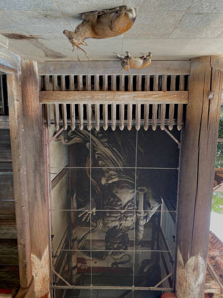 Statue derrière un treillis avec un cerf à proximité.