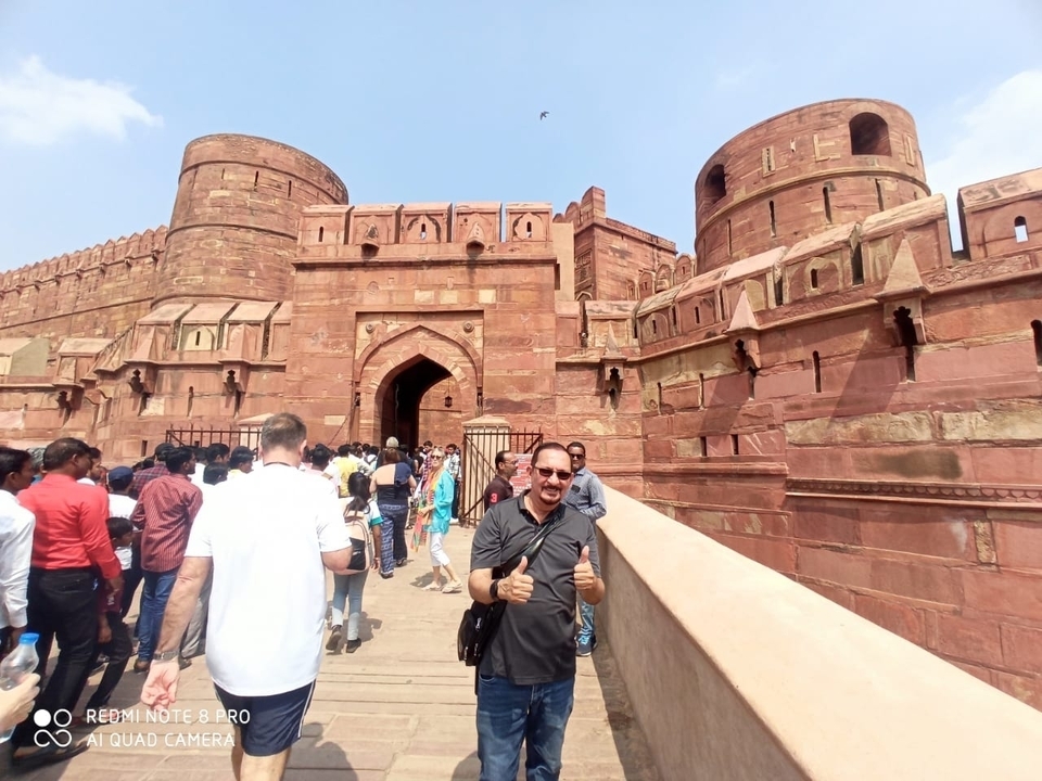 Un homme posant devant un grand fort rouge.