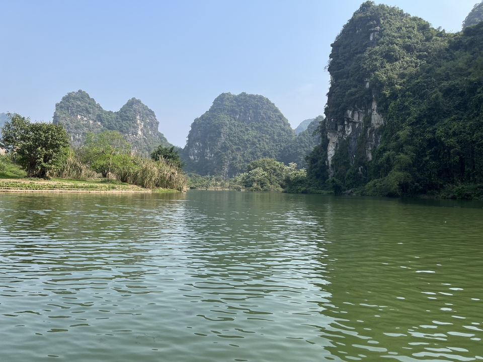 Des montagnes vertes et une rivière sereine sous un ciel clair.