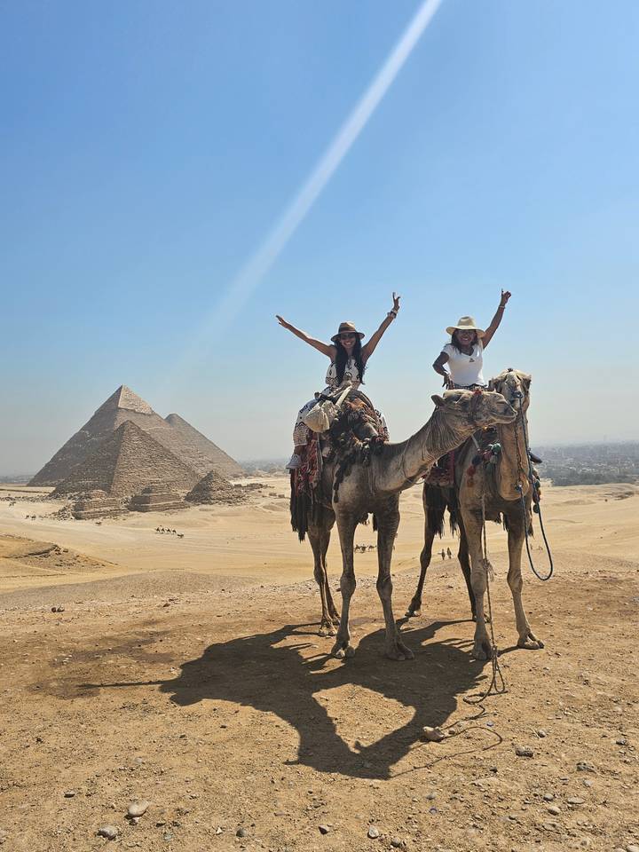 Menschen reiten auf Kamelen in der Nähe der Pyramiden in der Wüste.