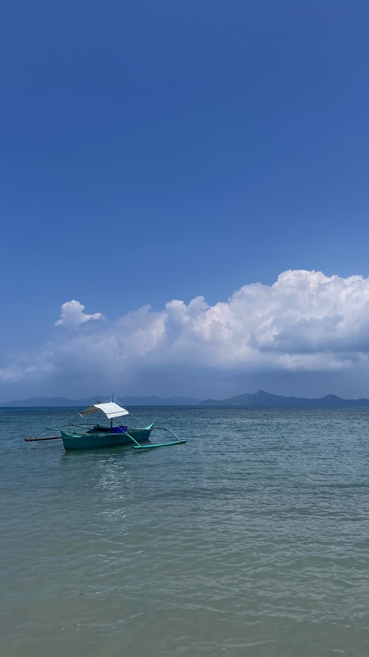 A small boat floating on clear blue ocean water with distant islands.