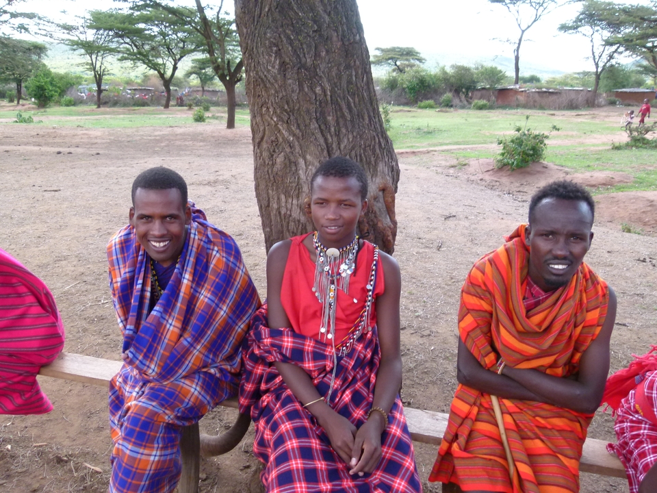 Trois personnes en tenue traditionnelle masaï assises sous un arbre.