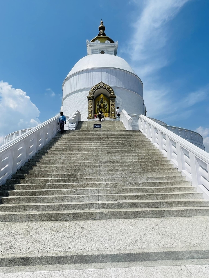 Steep steps leading up to a stupa with two people walking.