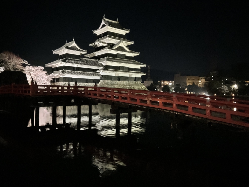 Château de Matsumoto illuminé la nuit avec un pont rouge au premier plan.