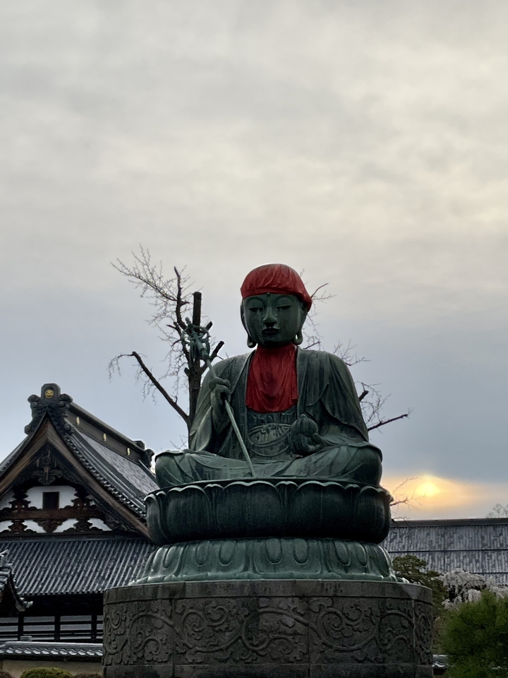 Une statue d'une figure assise en tenue traditionnelle avec un tissu rouge.