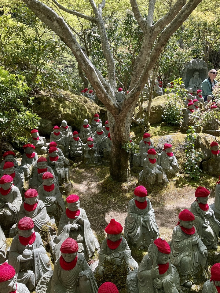 De nombreuses petites statues dans un espace jardin, chacune ornée d'un bonnet rouge et d'un bavoir.