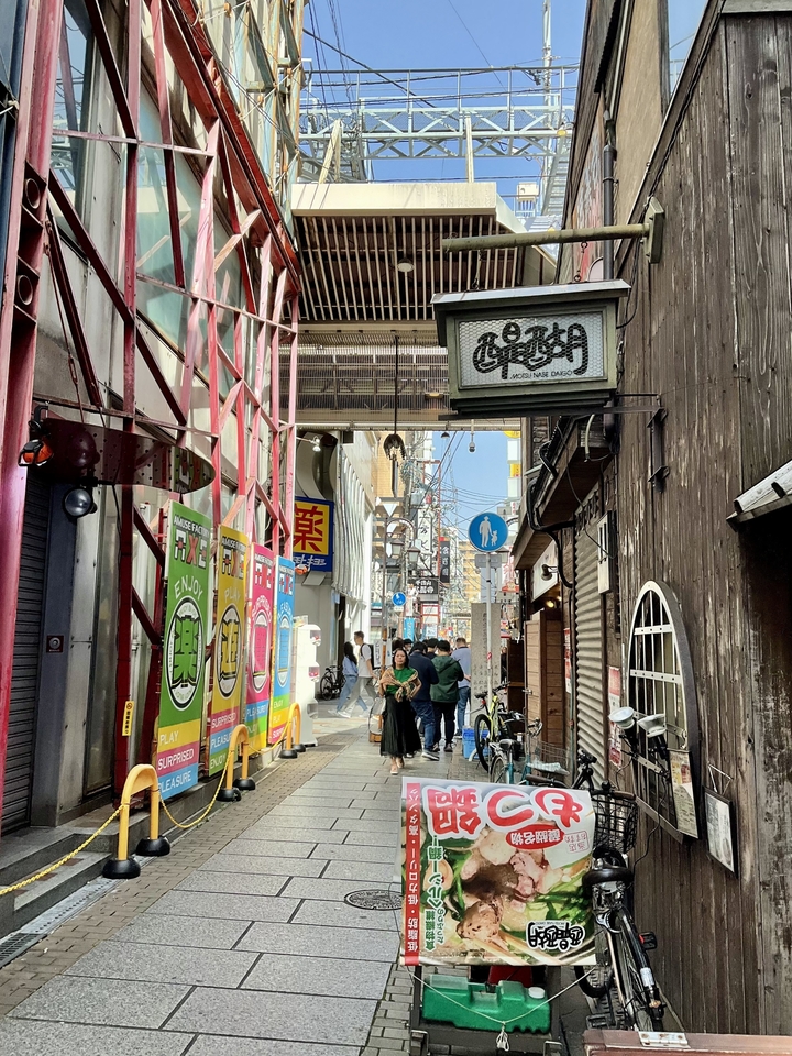 Une ruelle étroite avec des enseignes et des gens qui passent dans une ville.