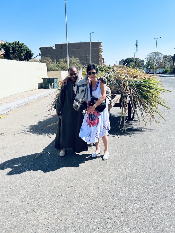 Deux personnes debout avec une charrette à âne remplie de légumes verts.