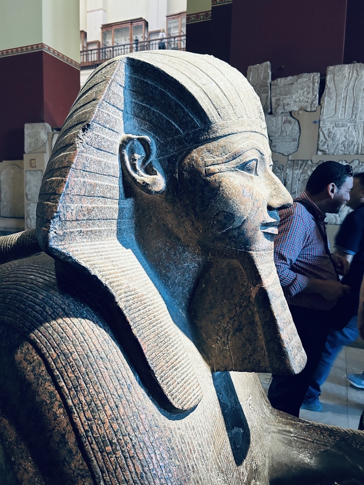 Plan rapproché d'une statue de pharaon avec des personnes en arrière-plan.