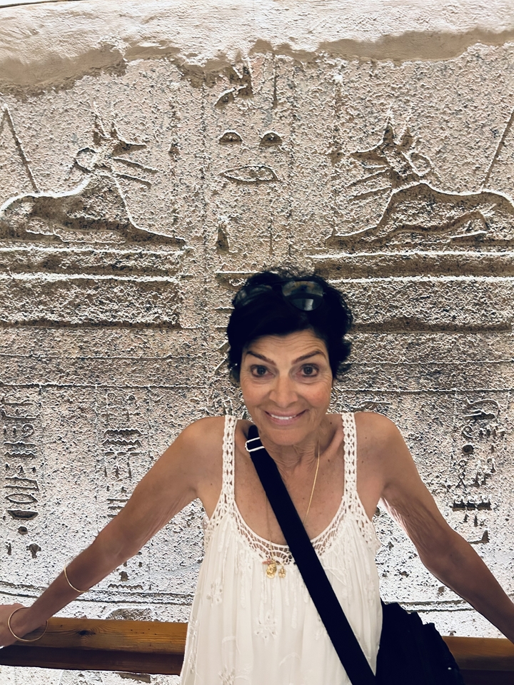 Personne souriante avec des sculptures anciennes en arrière-plan.