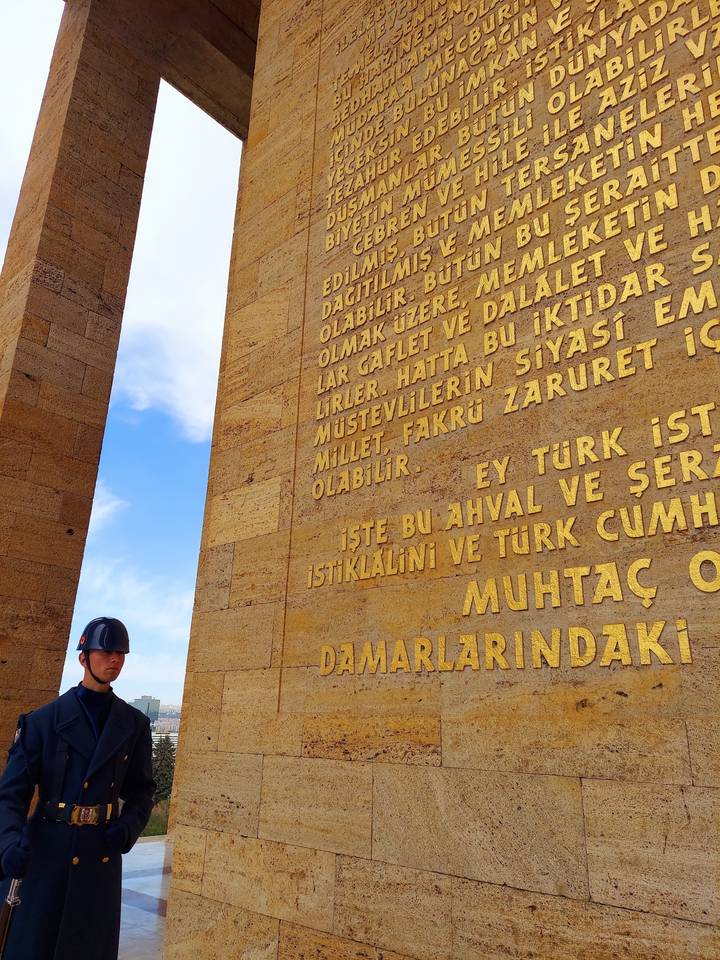 Garde debout à côté d'un mur avec du texte gravé sous un ciel bleu.