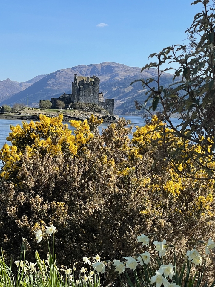 Château de pierre sur une île avec des montagnes en arrière-plan.