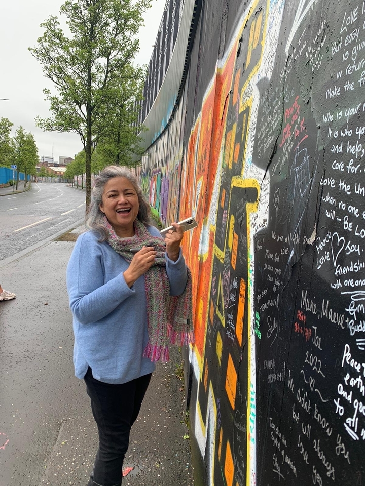 Femme souriante près d'une fresque murale colorée dans la rue.