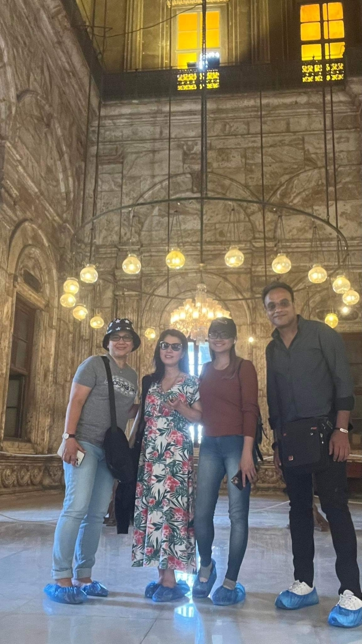 Quatre personnes posant dans un intérieur richement décoré avec des lustres.