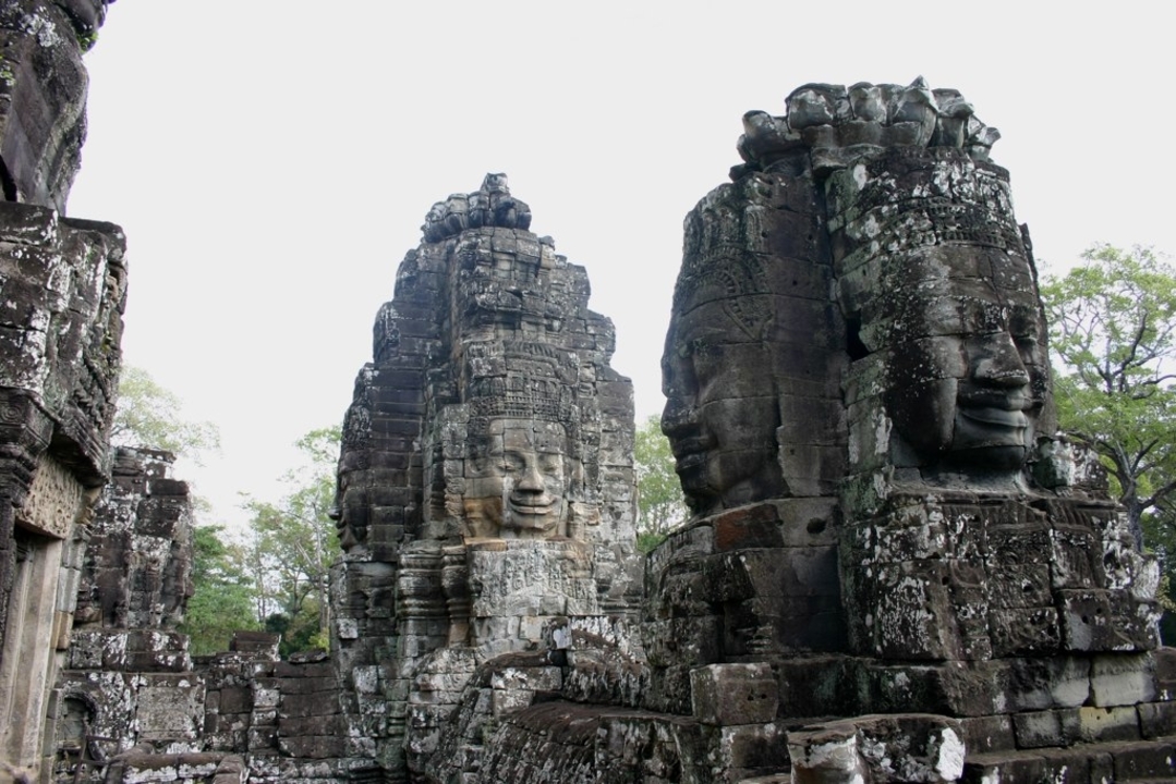 Steinschnitzereien von lächelnden Gesichtern an einem antiken Tempel.