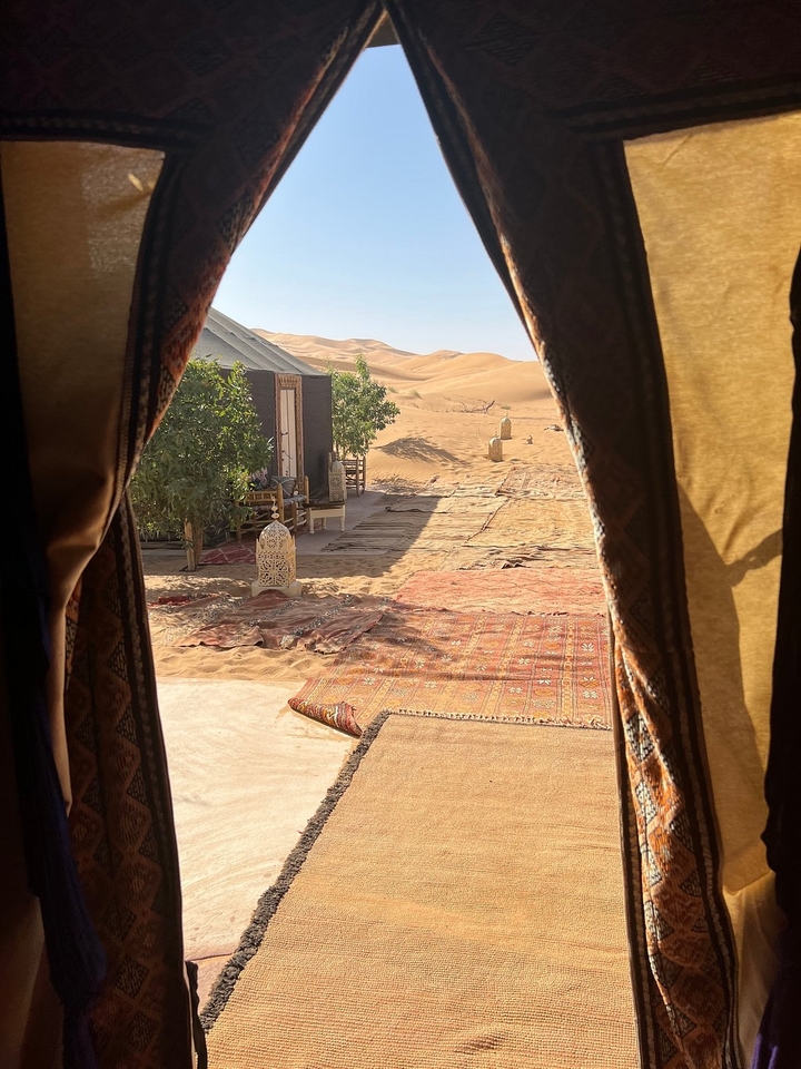 Vue depuis l'ouverture d'une tente donnant sur un campement dans le désert avec des dunes de sable.