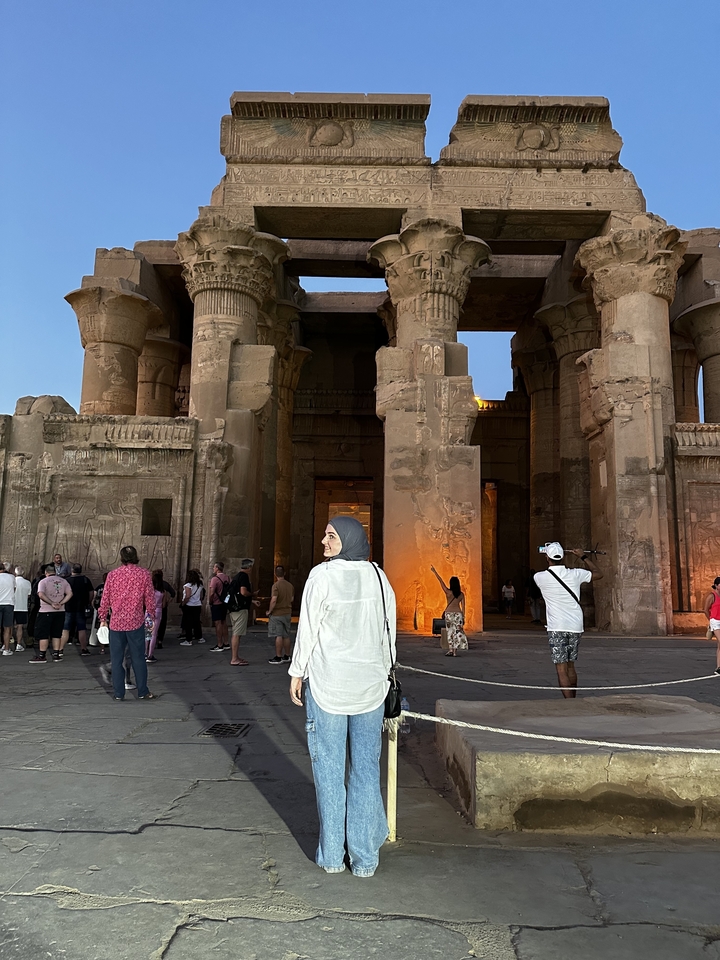 Des touristes devant des ruines égyptiennes avec des hiéroglyphes au crépuscule.