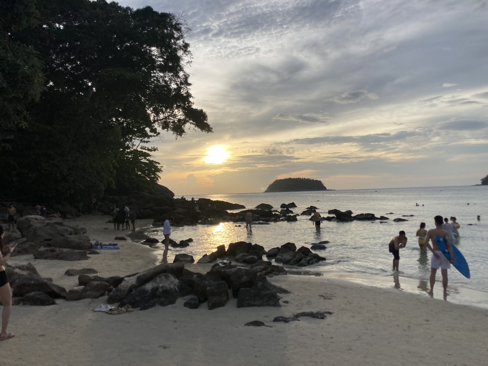 Scène de plage au coucher du soleil avec des nageurs et des surfeurs dans l'eau.