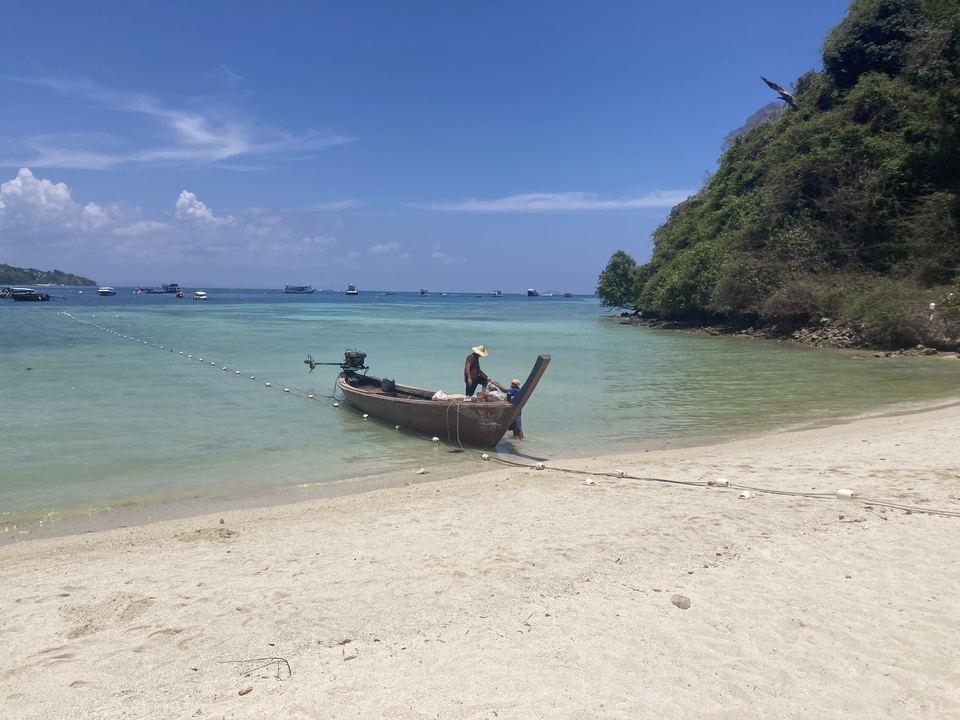 Femme dans un bateau à longue queue sur une plage de sable avec une eau claire.