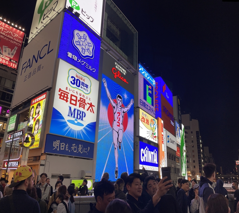 Publicités et enseignes éclairées dans un quartier urbain animé la nuit.