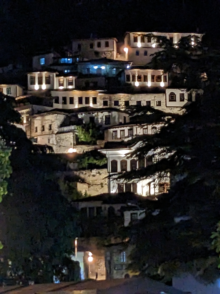 Maisons historiques à flanc de colline éclairées la nuit avec des arbres à proximité.